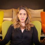 Katie Halper zittend in een groene stoel, kijkend naar de camera