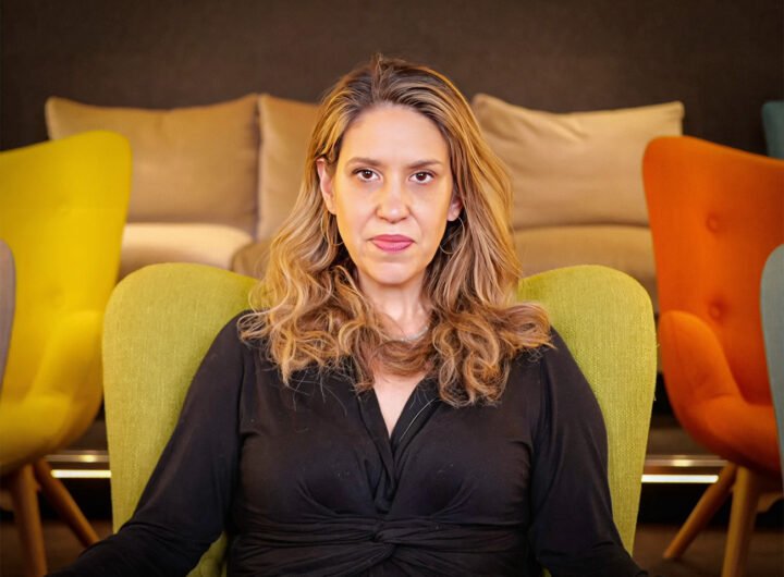 Katie Halper zittend in een groene stoel, kijkend naar de camera