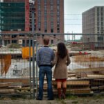 Twee mensen kijken naar een bouwplaats met flats in aanbouw achter een hek.