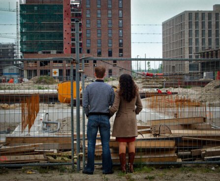 Twee mensen kijken naar een bouwplaats met flats in aanbouw achter een hek.