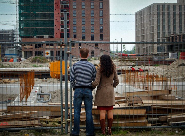 Twee mensen kijken naar een bouwplaats met flats in aanbouw achter een hek.
