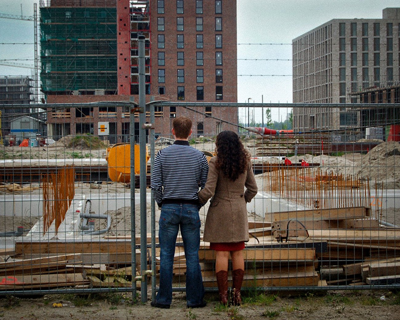 Twee mensen kijken naar een bouwplaats met flats in aanbouw achter een hek.