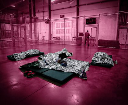 Kinderen in een Amerikaanse detentiehal liggen onder nooddekens binnen een omheind verblijf.