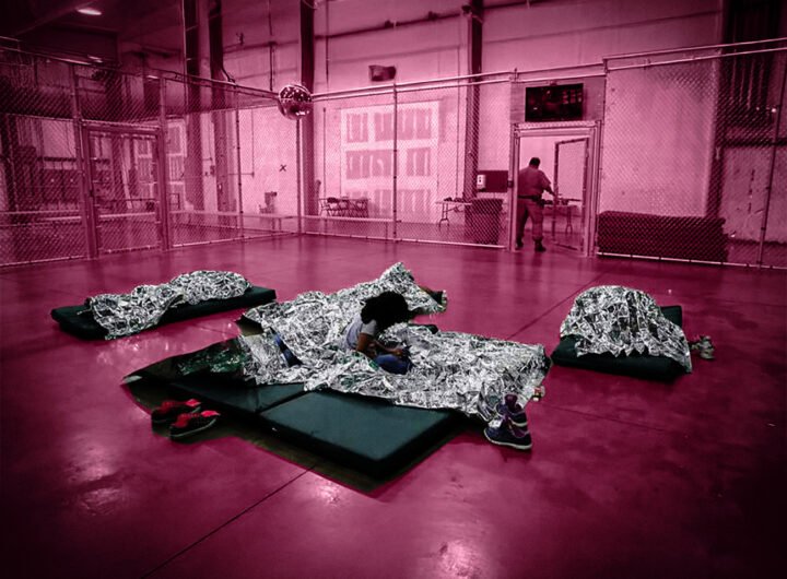 Kinderen in een Amerikaanse detentiehal liggen onder nooddekens binnen een omheind verblijf.