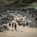 Mensen lopen door een verwoeste straat in Gaza tussen ingestorte gebouwen na zware bombardementen