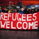 Groep mensen met spandoek ‘Refugees Welcome’ tijdens demonstratie bij zonsondergang.