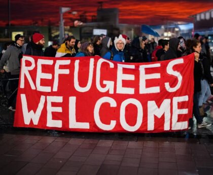 Groep mensen met spandoek ‘Refugees Welcome’ tijdens demonstratie bij zonsondergang.