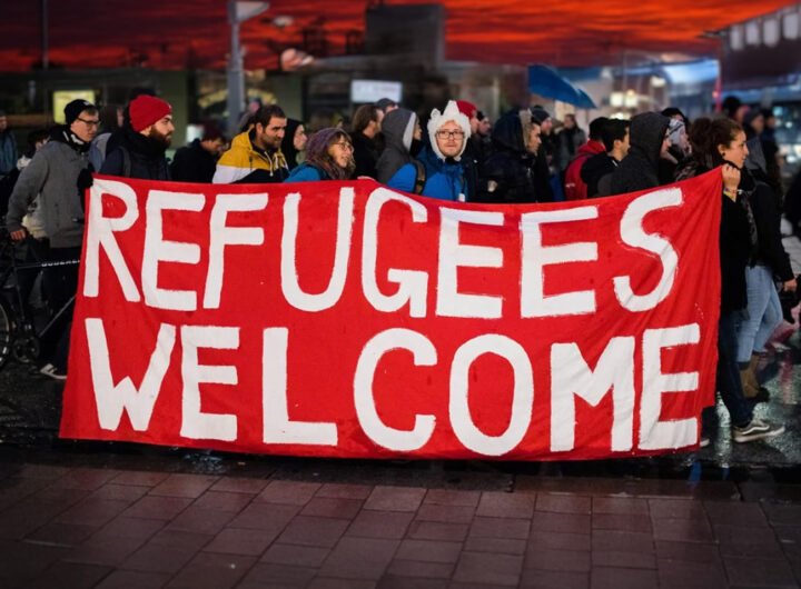 Groep mensen met spandoek ‘Refugees Welcome’ tijdens demonstratie bij zonsondergang.