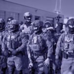 Groep zwaarbewapende federale agenten staat opgesteld tijdens een grootschalige operatie in een stedelijke omgeving.