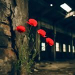 Rode wilde bloemen groeien door barsten in de muur van een donker, verlaten industrieel gebouw waar licht door gaten in het dak valt.