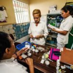 Drie zorgmedewerkers in een Venezolaanse kliniek sorteren medicijnen aan een tafel vol schaarse voorraden.