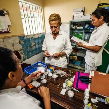 Drie zorgmedewerkers in een Venezolaanse kliniek sorteren medicijnen aan een tafel vol schaarse voorraden.