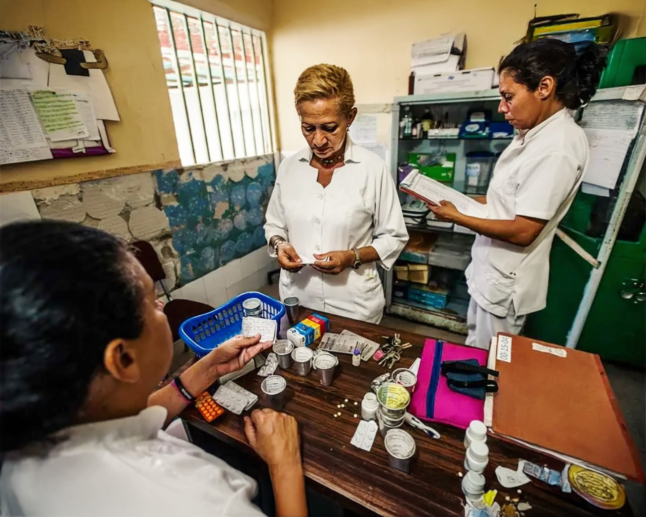Drie zorgmedewerkers in een Venezolaanse kliniek sorteren medicijnen aan een tafel vol schaarse voorraden.