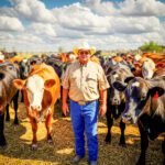 Amerikaanse veehouder staat tussen runderen op een erf, symbool voor voedselproductie onder druk van markt en prijsbeleid.