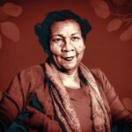 Portret van bell hooks in 2018, zittend en kijkend naar de camera, tegen een warme achtergrond met bladmotieven.