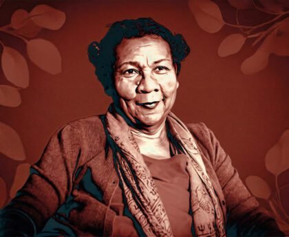 Portret van bell hooks in 2018, zittend en kijkend naar de camera, tegen een warme achtergrond met bladmotieven.