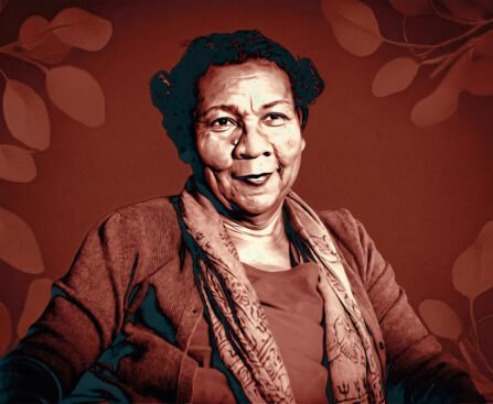 Portret van bell hooks in 2018, zittend en kijkend naar de camera, tegen een warme achtergrond met bladmotieven.