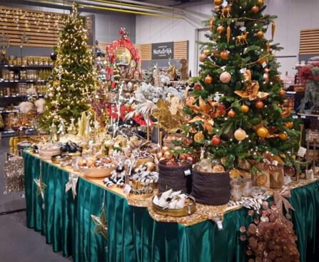 Rijk gedecoreerde kerstbomen en feesttafels vol kerstdecoratie in een winkel, met nadruk op overvloed, goudkleurige ornamenten en koopwaar.