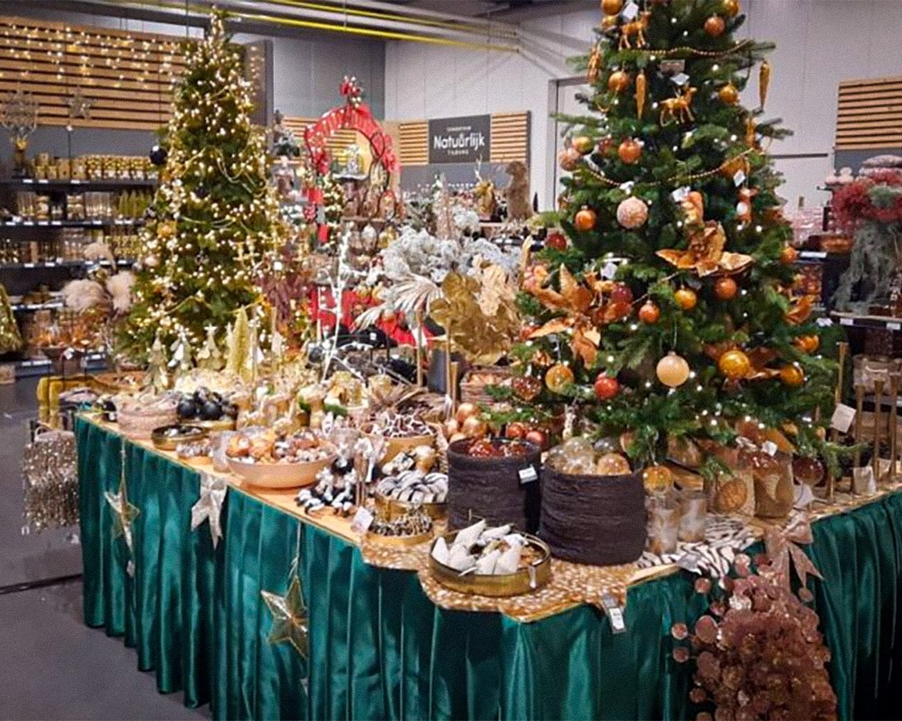 Rijk gedecoreerde kerstbomen en feesttafels vol kerstdecoratie in een winkel, met nadruk op overvloed, goudkleurige ornamenten en koopwaar.