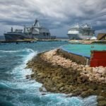 Militair schip en cruiseschip aangemeerd bij Willemstad, Curacao, terwijl donkere wolken zich samenpakken boven zee.
