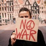 Persoon houdt een kartonnen bord met de tekst “No War” omhoog in een Amsterdamse straat