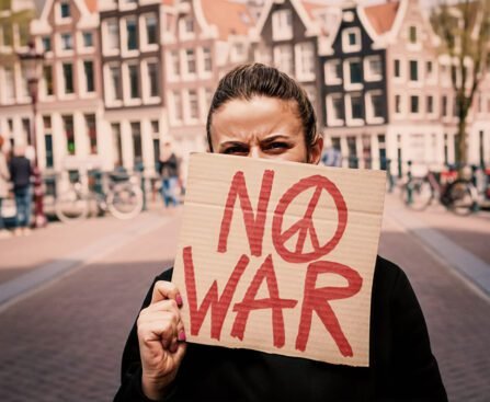Persoon houdt een kartonnen bord met de tekst “No War” omhoog in een Amsterdamse straat