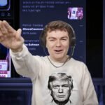Jonge extreemrechtse influencer met koptelefoon steekt arm omhoog tijdens livestream, met schermen vol sociale media en politieke trending topics op de achtergrond.