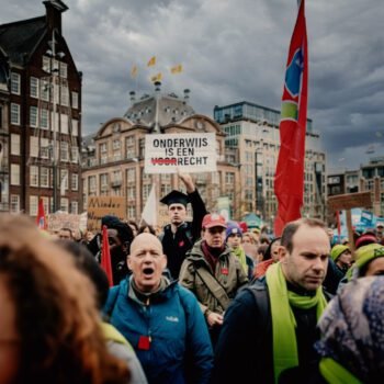 Studenten en docenten op de Dam tijdens een protest tegen bezuinigingen op het hoger onderwijs, met spandoeken en uitzicht op het plein.