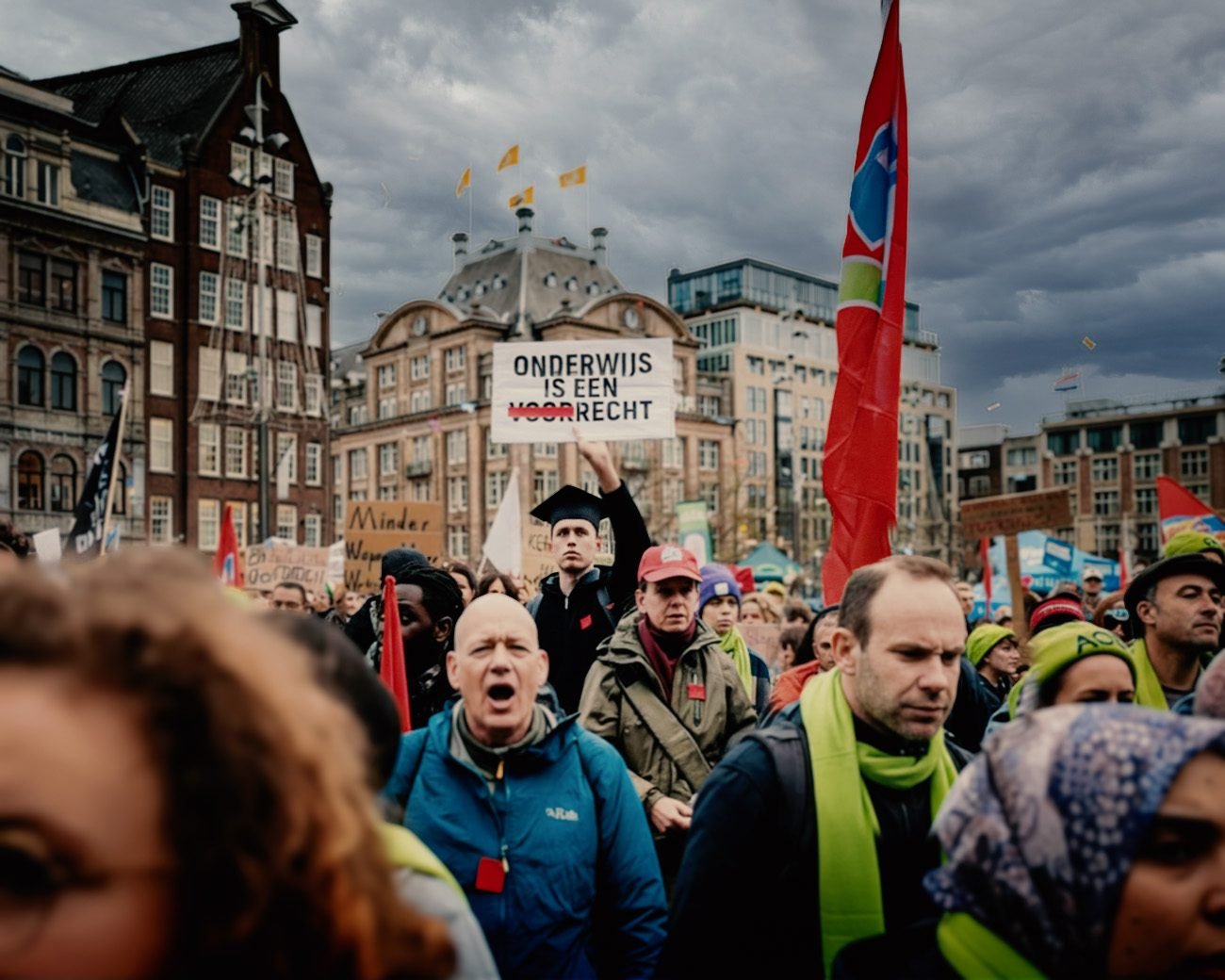 Studenten en docenten op de Dam tijdens een protest tegen bezuinigingen op het hoger onderwijs, met spandoeken en uitzicht op het plein.
