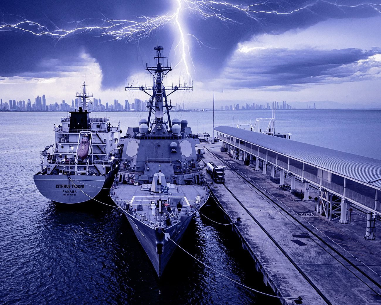 Een Amerikaans marineschip naast een vrachtschip aan de kade in Panama City, met onweer boven de skyline.