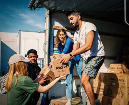 Vrijwilligers laden dozen met benodigdheden uit een vrachtwagen om ze te verdelen onder buurtgenoten die steun nodig hebben.