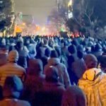 Grote groep demonstranten loopt ’s nachts door een verlichte straat tijdens protesten in Iran