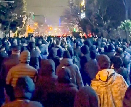 Grote groep demonstranten loopt ’s nachts door een verlichte straat tijdens protesten in Iran