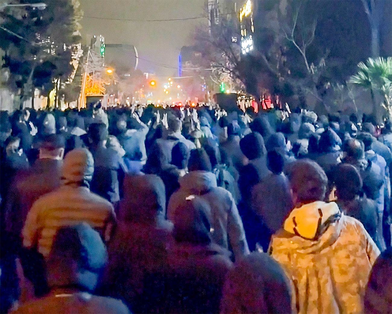 Grote groep demonstranten loopt ’s nachts door een verlichte straat tijdens protesten in Iran