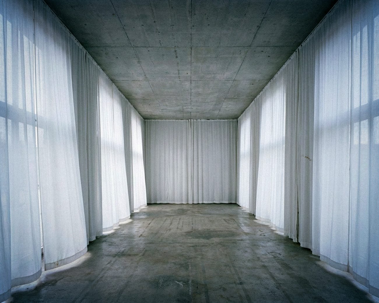 Lege institutionele ruimte met betonnen plafond en witte doeken die een tijdelijke morele façade suggereren