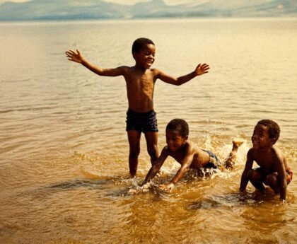 Zwarte kinderen spelen in ondiep water aan een kust of rivier in de Verenigde Staten, een plek waar families generaties lang samenkwamen en kinderen leerden zwemmen.