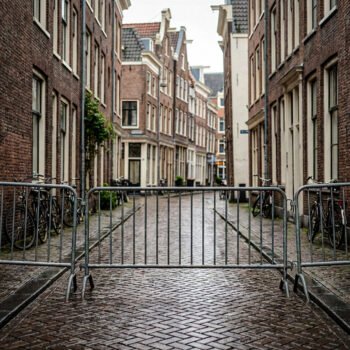Lege Amsterdamse straat met metalen dranghekken die de doorgang blokkeren tussen bakstenen huizen en fietsen.