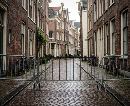 Lege Amsterdamse straat met metalen dranghekken die de doorgang blokkeren tussen bakstenen huizen en fietsen.