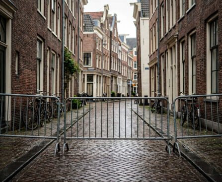 Lege Amsterdamse straat met metalen dranghekken die de doorgang blokkeren tussen bakstenen huizen en fietsen.