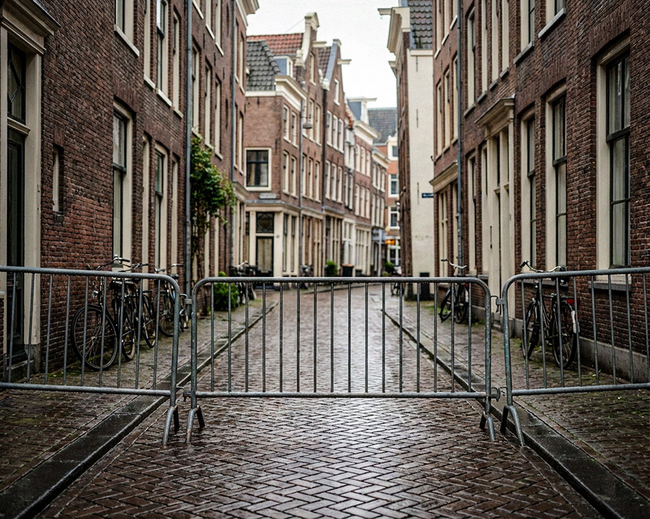 Lege Amsterdamse straat met metalen dranghekken die de doorgang blokkeren tussen bakstenen huizen en fietsen.