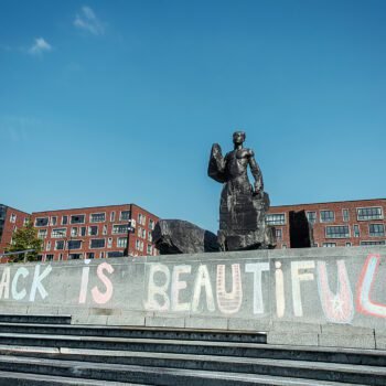 Standbeeld van Anton de Kom op het Anton de Komplein met op de trappen de graffiti Black is Beautiful