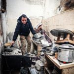 Man staat in een beschadigde keuken in Gaza en verzamelt kookgerei tussen puin en ingestorte muren