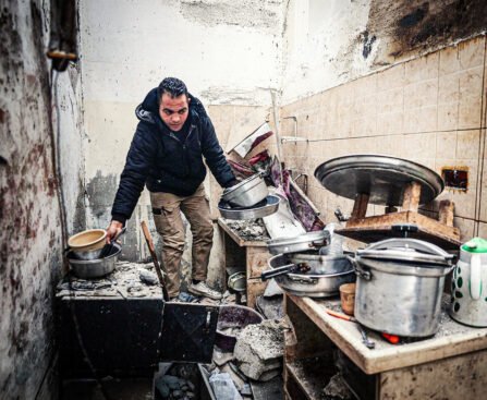 Man staat in een beschadigde keuken in Gaza en verzamelt kookgerei tussen puin en ingestorte muren