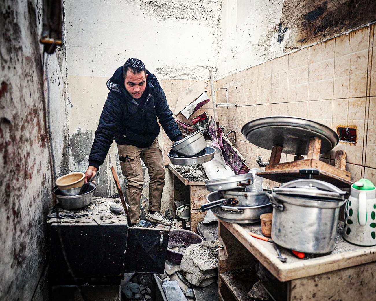 Man staat in een beschadigde keuken in Gaza en verzamelt kookgerei tussen puin en ingestorte muren