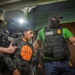 Gemaskerde agenten van U.S. Customs and Border Protection arresteren een man bij een woning terwijl zij hem vasthouden aan beide armen.