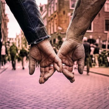 Twee mannen houden elkaars hand vast op een drukke straat in Amsterdam.