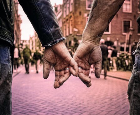 Twee mannen houden elkaars hand vast op een drukke straat in Amsterdam.