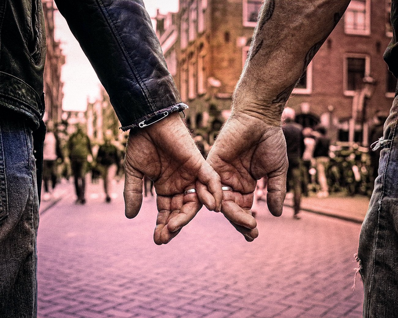 Twee mannen houden elkaars hand vast op een drukke straat in Amsterdam.