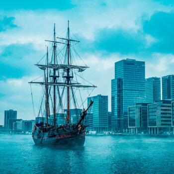 Historisch VOC-schip op het IJ met moderne kantoortorens van Amsterdam op de achtergrond