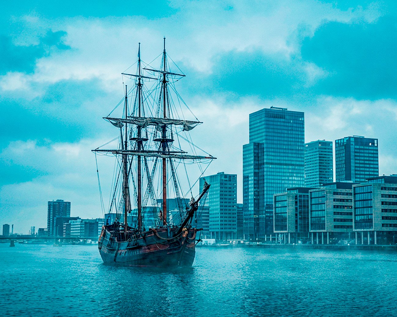 Historisch VOC-schip op het IJ met moderne kantoortorens van Amsterdam op de achtergrond